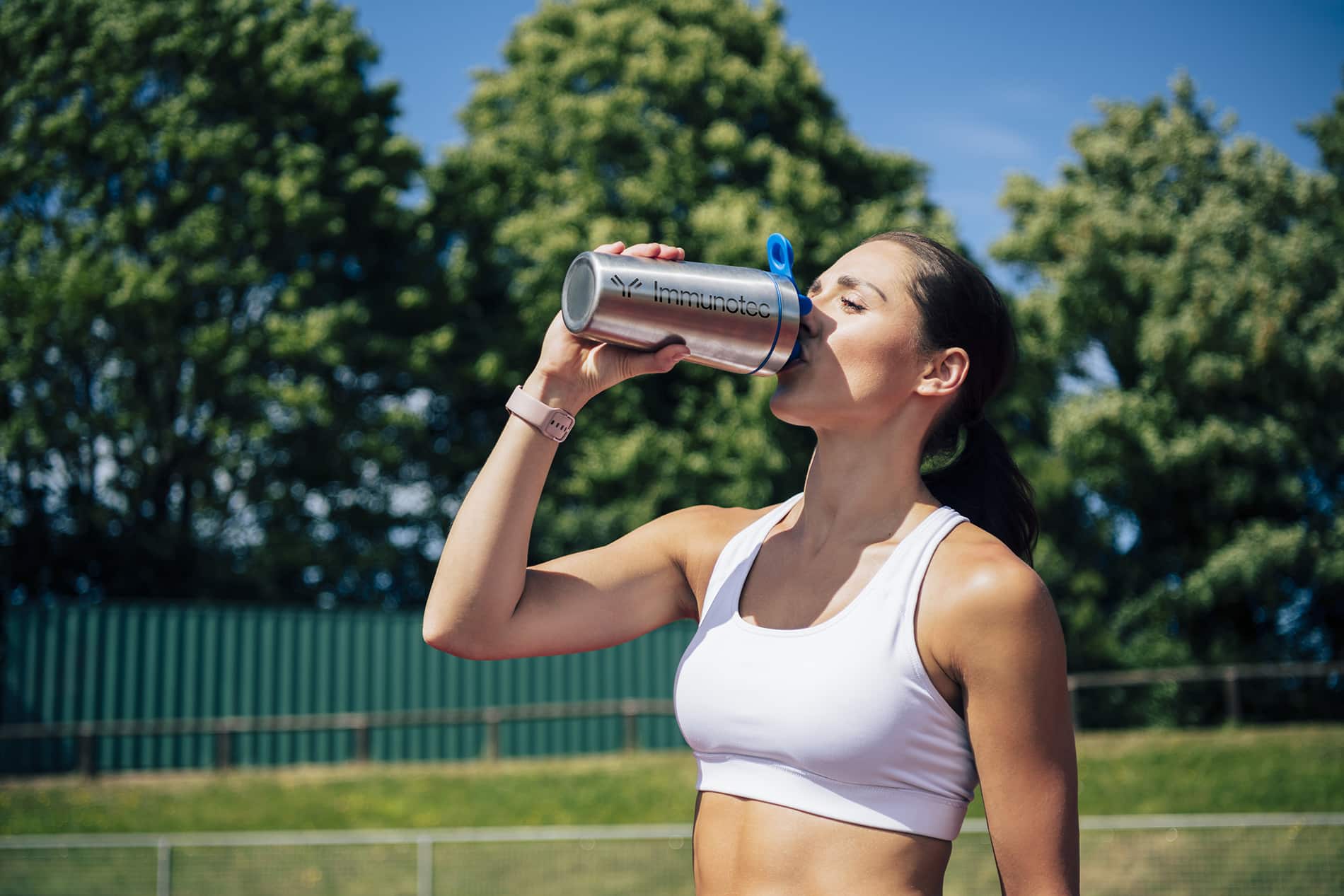 Mid adult Caucasian female athlete pausing from training for protein refreshment on warm summer day.